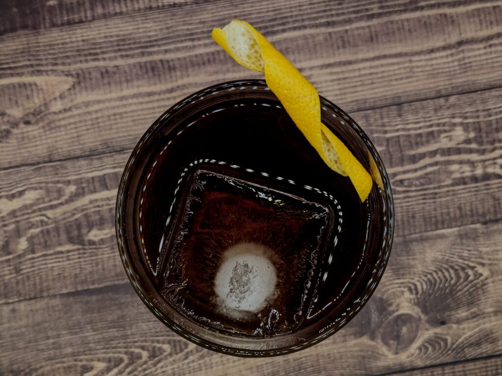 Dark drink with large ice cube and lemon peel garnish