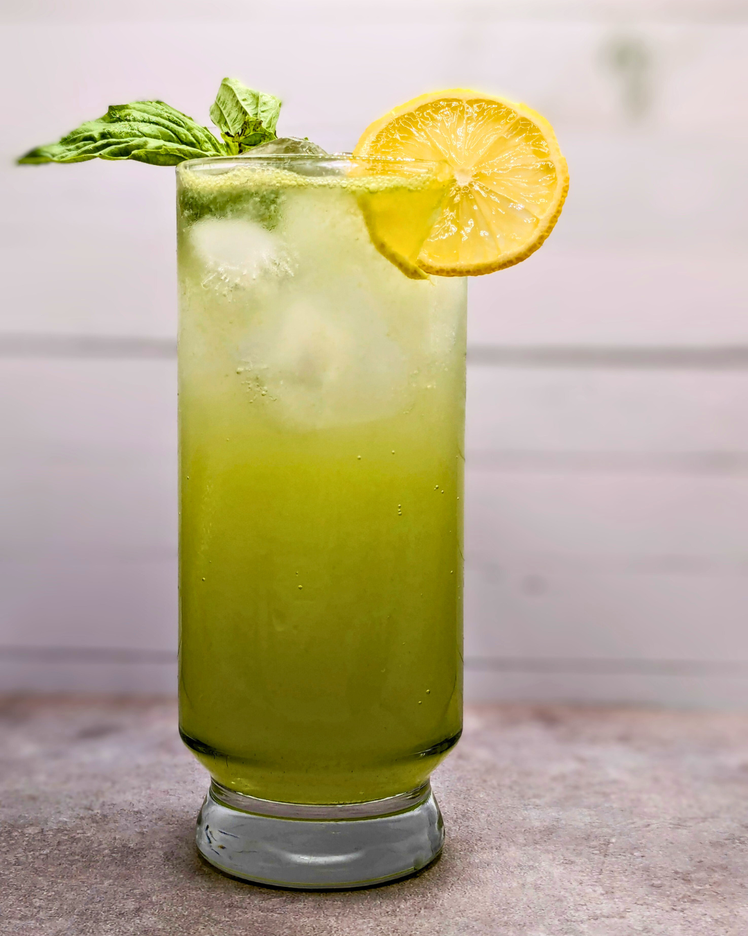 A green cocktail made with cucumbers and basil garnished with fresh mint and a lemon wheel