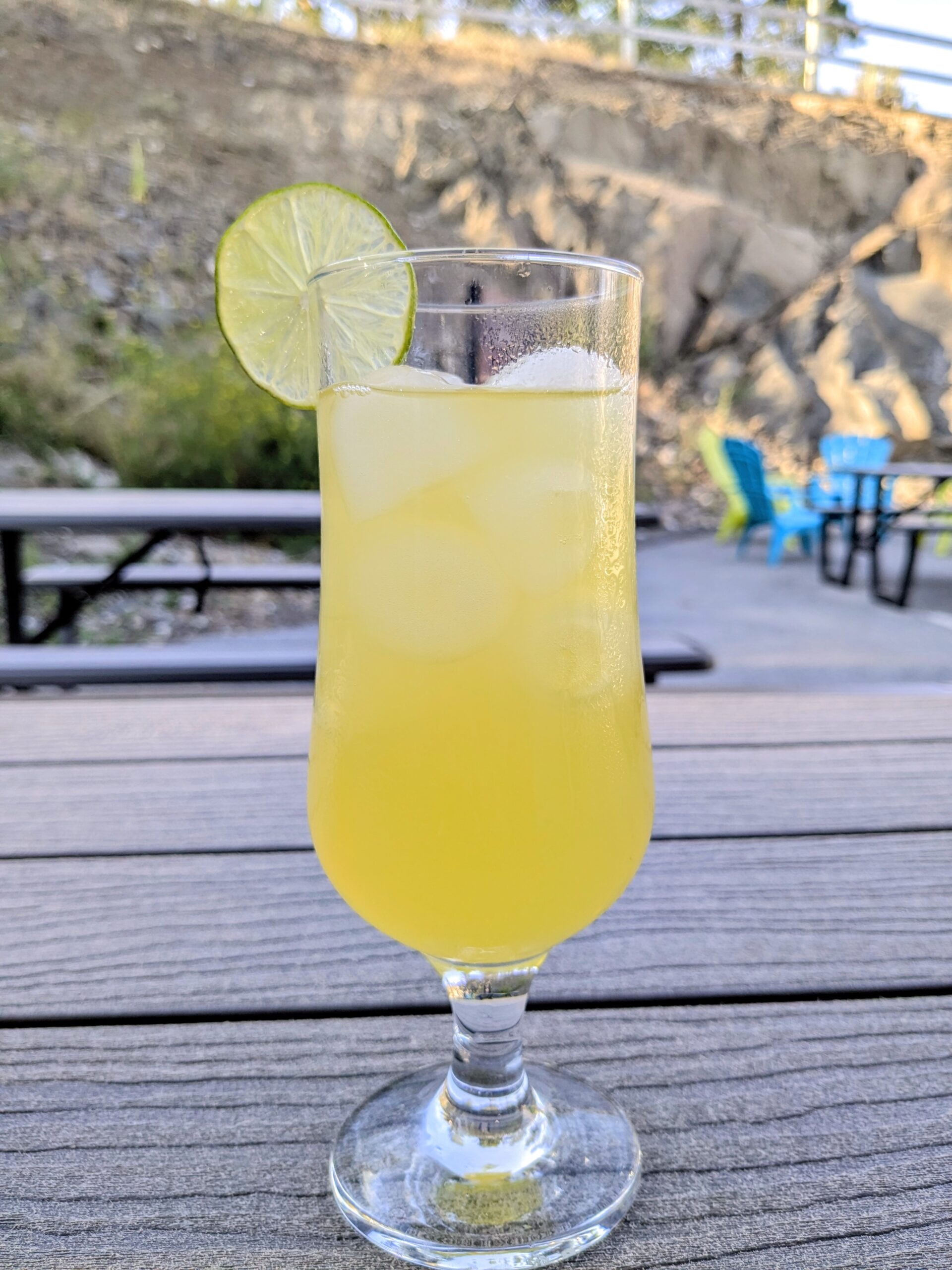 A bright yellow cocktail over ice, garnished with a lime wheel, enjoyed outdoors in warm sunlight